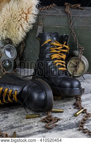 Leather Boots With Rusted Chains And Bullet Shells With Military Gas Mask And Fur Coat In Background