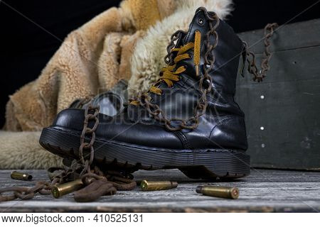 Leather Boot With Rusted Chains And Bullet Shells With Military Gas Mask And Fur Coat In Background