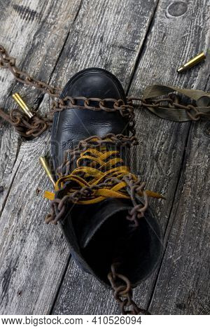 Leather Boot With Rusted Chains And Bullet Shells Resting On Wooden Table