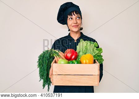 Beautiful brunettte woman chef holding fresh veggetables smiling looking to the side and staring away thinking. 