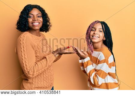 Beautiful african american mother and daughter wearing wool winter sweater pointing aside with hands open palms showing copy space, presenting advertisement smiling excited happy 