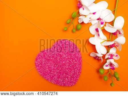 Pink Small Stones In A Heart-shaped Mold With A Flower On Top Of The Background On An Orange Backgro