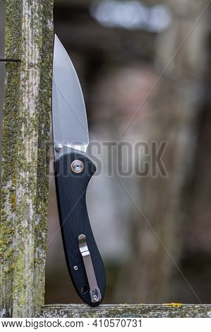 A Folding Knife With A Black Handle And A Clip. Photo Of A Knife On The Street. Vertical Frame.