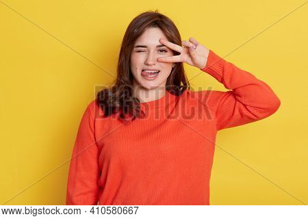 European Dark Haired Lady With Funny Expression, Posing Isolated Over Yellow Background, Showing Ton
