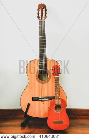 Classic Six-string Wooden Guitar And Hawaiian Four-string Guitar Ukulele Stand Against The Wall. Com