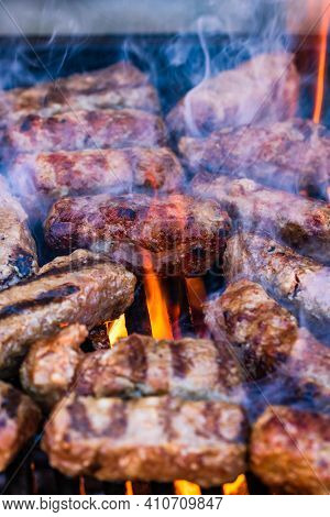 Preparing Meat Rolls Called Mici Or Mititei On Barbecue. Close Up Of Grill With Burning Fire With Fl