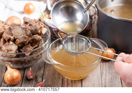 Passing The Bone Broth Through A Sieve. Concentrated Bone Broth In A Bowl