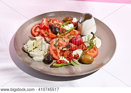 Tomato, olives and mozzarella salad . Restaurant appetizer plate on white table with pink wall. Day sunlight with hard shadow of fern palm leaves. Summer or spring restaurant food concept
