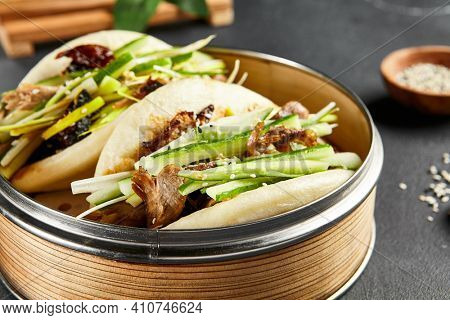 Bao bun with roast duck. Bamboo steamer on dark slate table. Chinese, asian, authentic food concept.