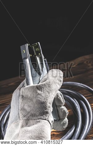 A Welder In White Welding Gloves Holds A Wire With A Ground Terminal In His Hand. Studio Photo In Ha