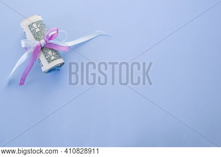 Rolled Up Dollar Bills Secured By Blue And Pink Ribbon With Copy Space On A Blue Background.