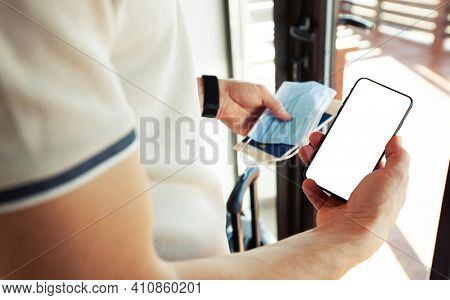 The man holding the mobile phone with empty space as a mockup for digital vaccination certificate in one hand and passport, mask and ticket in another one