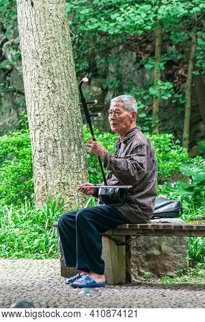 Guilin, China - May 11, 2010: Seven Star Park. Man Sitting On Bench Plays The Erhu Or Chinese Violin
