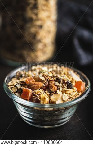 Beakfast cereals in bowl. Healthy muesli with oat flakes, nuts and raisins on black table.