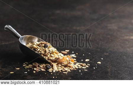 Beakfast cereals in scoop. Healthy muesli with oat flakes, nuts and raisins on black table.