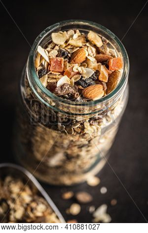 Beakfast cereals in jar. Healthy muesli with oat flakes, nuts and raisins on black table.