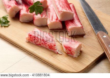 Appetizing crab sticks on wooden cutting board is laying on light table. Selective focus on cut crab stick