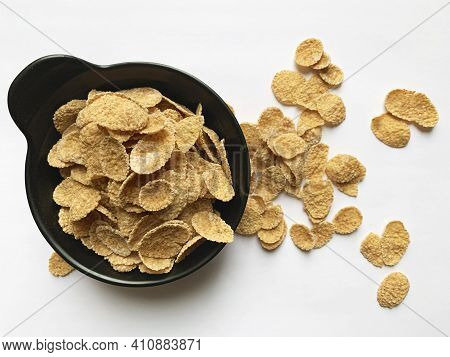 Multi-cereal Flakes In A Black Cup With Scattered Flakes On White Background. Top View.