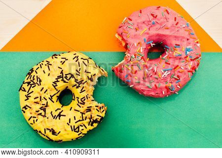 Two Bright Nibbled Doughnuts Lie On A Multicolored Background