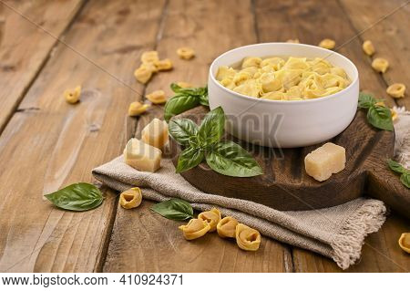 Tortellini Mignon On A Wooden Board With Basil And Parmesan. Specialties Of The Cuisine From Bologna
