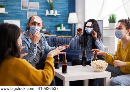 Cheerful Friends With Sticky Notes On Foreheads Playing Name Game With Beer Popcron Keeping Social D