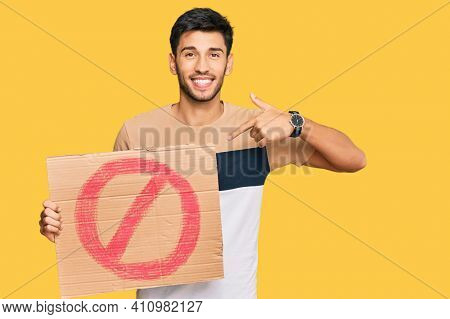 Young handsome man holding prohibited warning banner pointing finger to one self smiling happy and proud 
