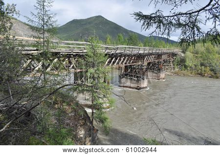 Wooden Bridge In Yakutia Across The Mountain River.