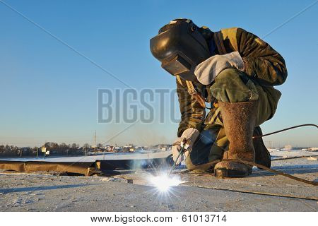 welder working with electrode at arc werding in construction site winter outdoors