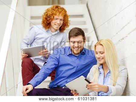 business, technology and startup concept - smiling creative team with tablet pc computer sitting on staircase