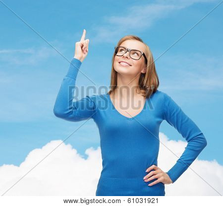 advertisement concept - attractive young woman in casual clothes and black eyeglasses pointing her finger up