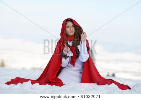 beautiful woman with red cloak sitting on the snow in winter