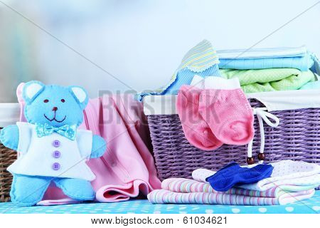 Pile of baby clothes  in basket, on table on color background