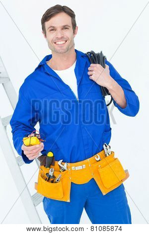 Portrait of happy electrician with wire roll and multimeter over white background