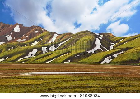 Magnificent colorful mountains. Reserve Landmannalaugar, Iceland. Green moss on smooth slopes and white spots snowfields in the gullies