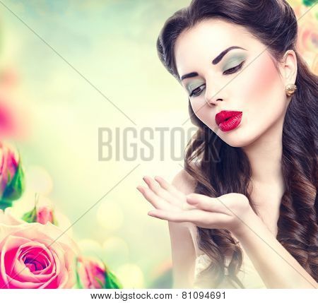 Retro woman portrait in beauty pink roses garden. Beautiful Vintage styled girl with flowers. Perfect makeup and hairstyle. Gorgeous model lady. Red Lips. Luxury Make up and Hair. Vogue Style