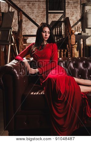 elegant sensual young woman in red dress sitting on leather sofa