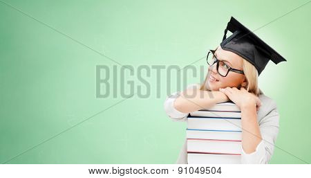 education, happiness, graduation and people concept - picture of happy student in mortar board cap with stack of books daydreaming over green background
