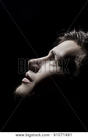 Portrait of a student,man side profile looking up lighted on a half face isolated on black
