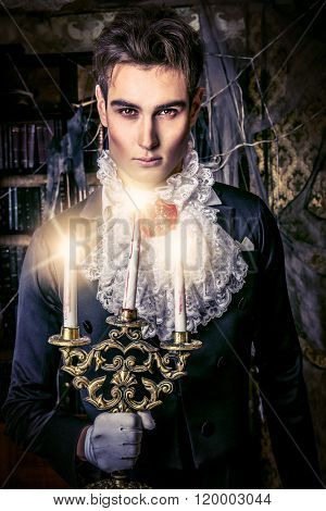 Handsome vampire man wearing elegant tailcoat stands in the old medieval castle. Halloween.