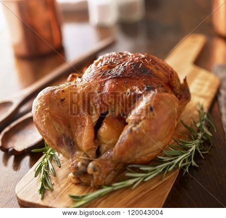 rotisserie chicken on wooden serving tray with herbs and rosemary