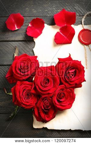 Fresh red roses buds in shape of heart with blank present card on wooden background