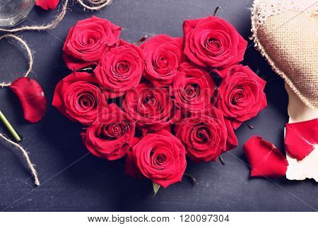 Fresh red roses buds in shape of heart with rope on black textured background