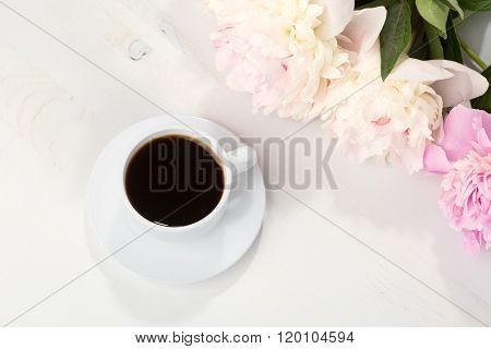 Still life with cup of coffee and flowers (peonies) on white wooden table.