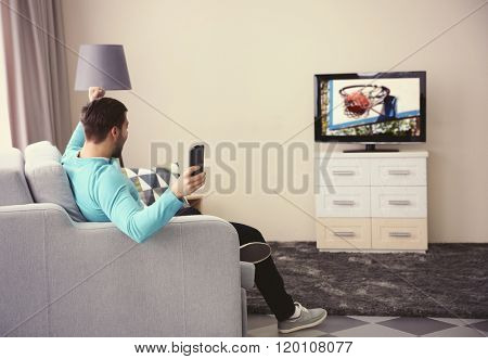 Young handsome man watching TV on a sofa at home