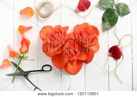 Fresh red roses buds in shape of heart with rope and scissors on wooden background