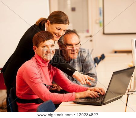 Young Woman Teaching Elderly Couple Of Computer Skills. Intergenerational Transfer Of Knowledge.