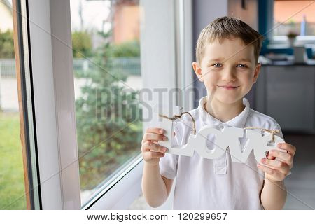 Happy little boy holding a wooden inscription with the word 