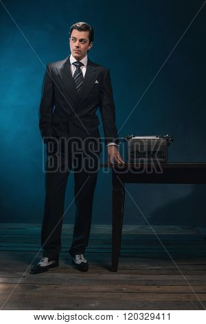 Vintage 1940S Business Man In Suit And Tie Standing Next To Desk With Typewriter.