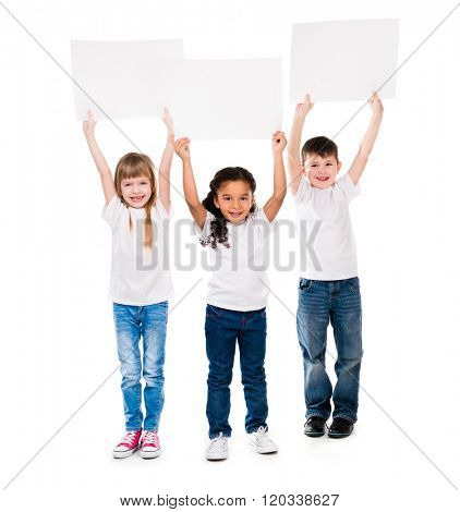 three cheeerful children holding en empty paper sheet above themselves isolated on white background