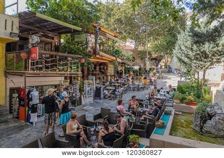 Tourists sit in summer cafe on street of Spili town at Crete island
